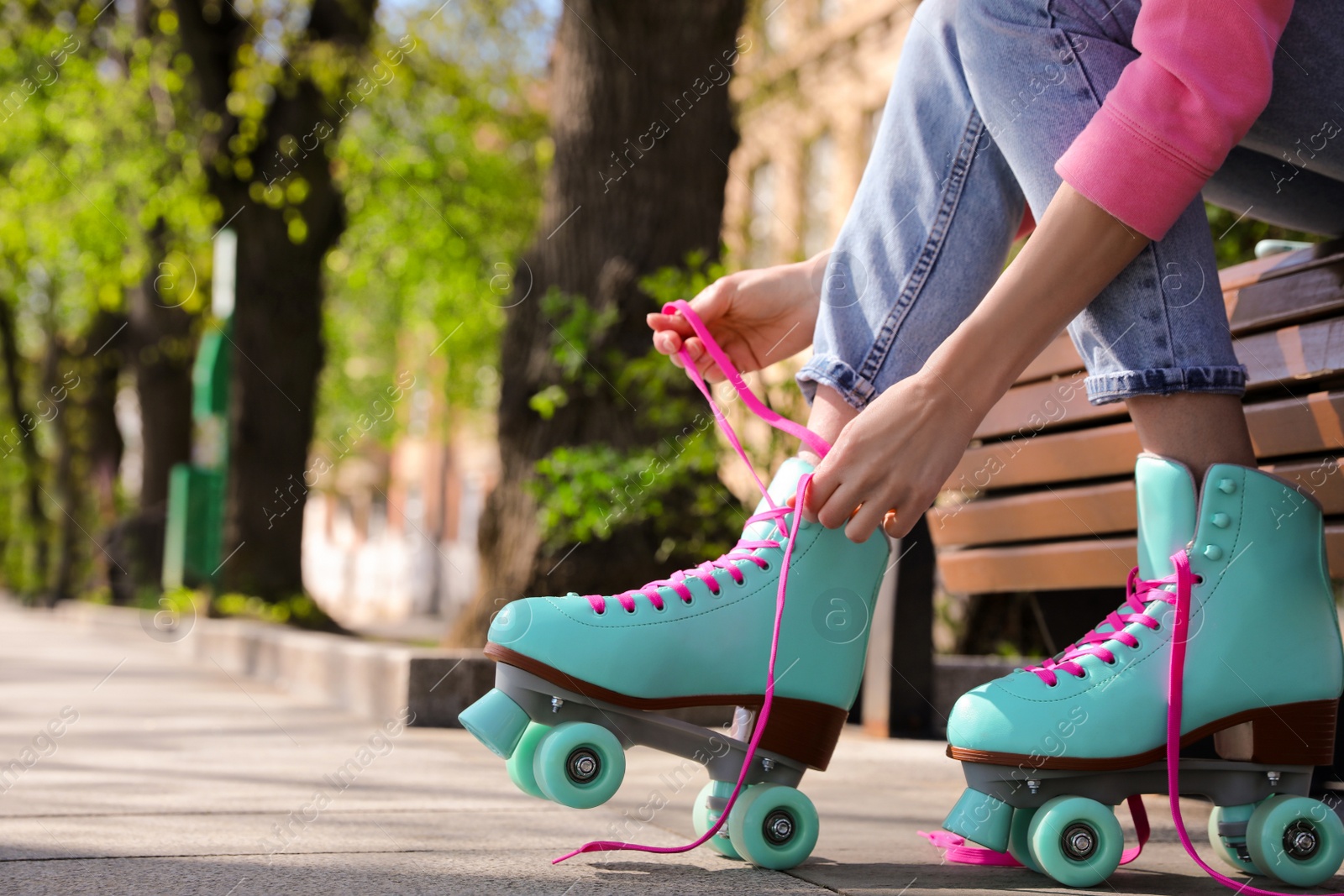 Photo of Woman lacing roller skates while sitting on bench outdoors, closeup