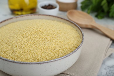 Photo of Bowl of raw couscous on white marble table, closeup