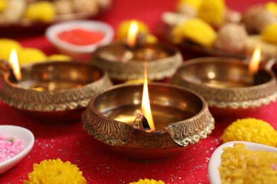 Photo of Diwali celebration. Diya lamps and chrysanthemum flowers on shiny red table, closeup