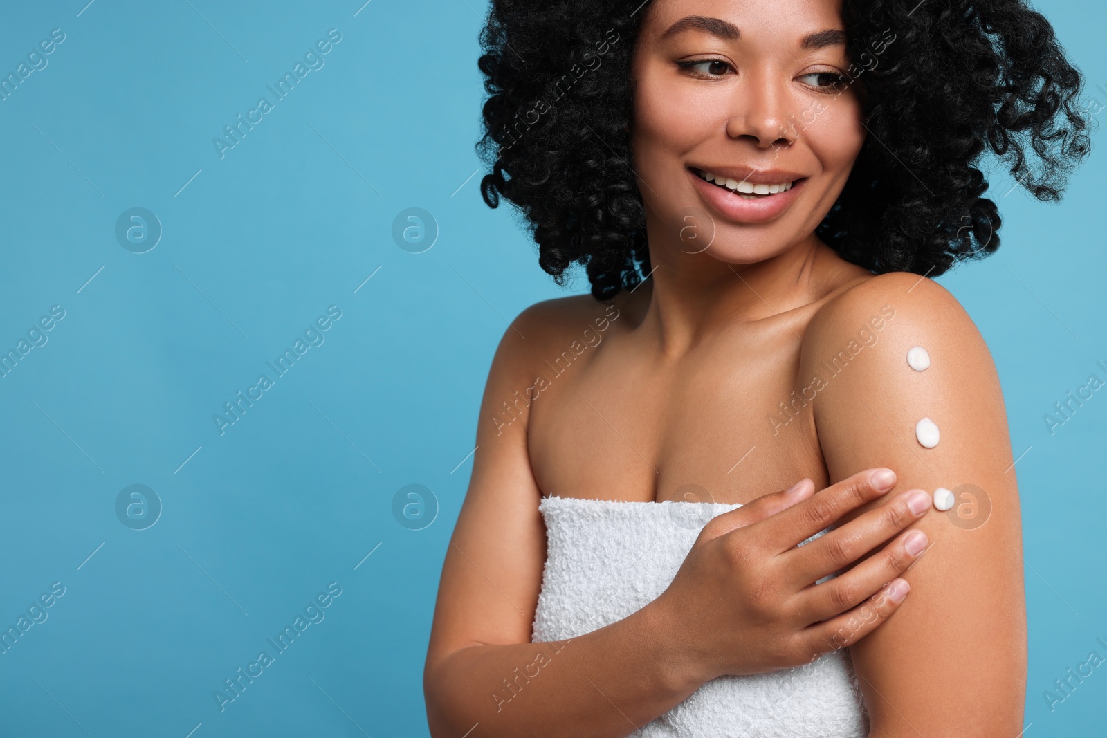 Photo of Young woman applying body cream onto shoulder on light blue background. Space for text