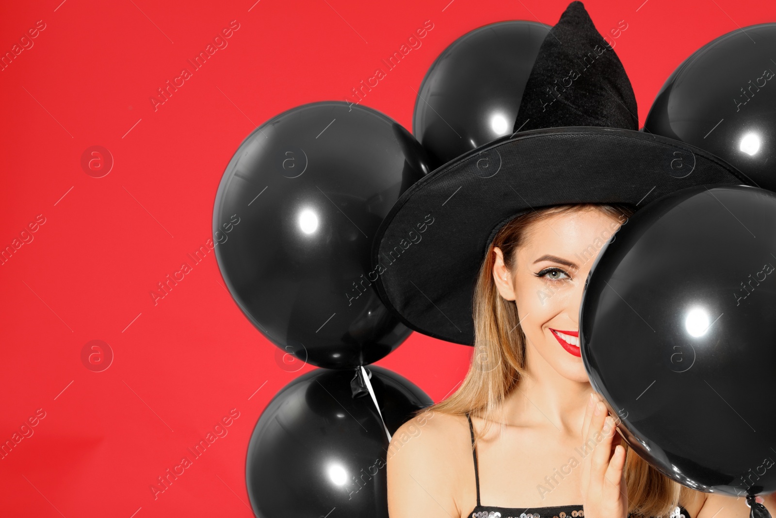 Photo of Beautiful woman wearing witch costume with balloons for Halloween party on red background