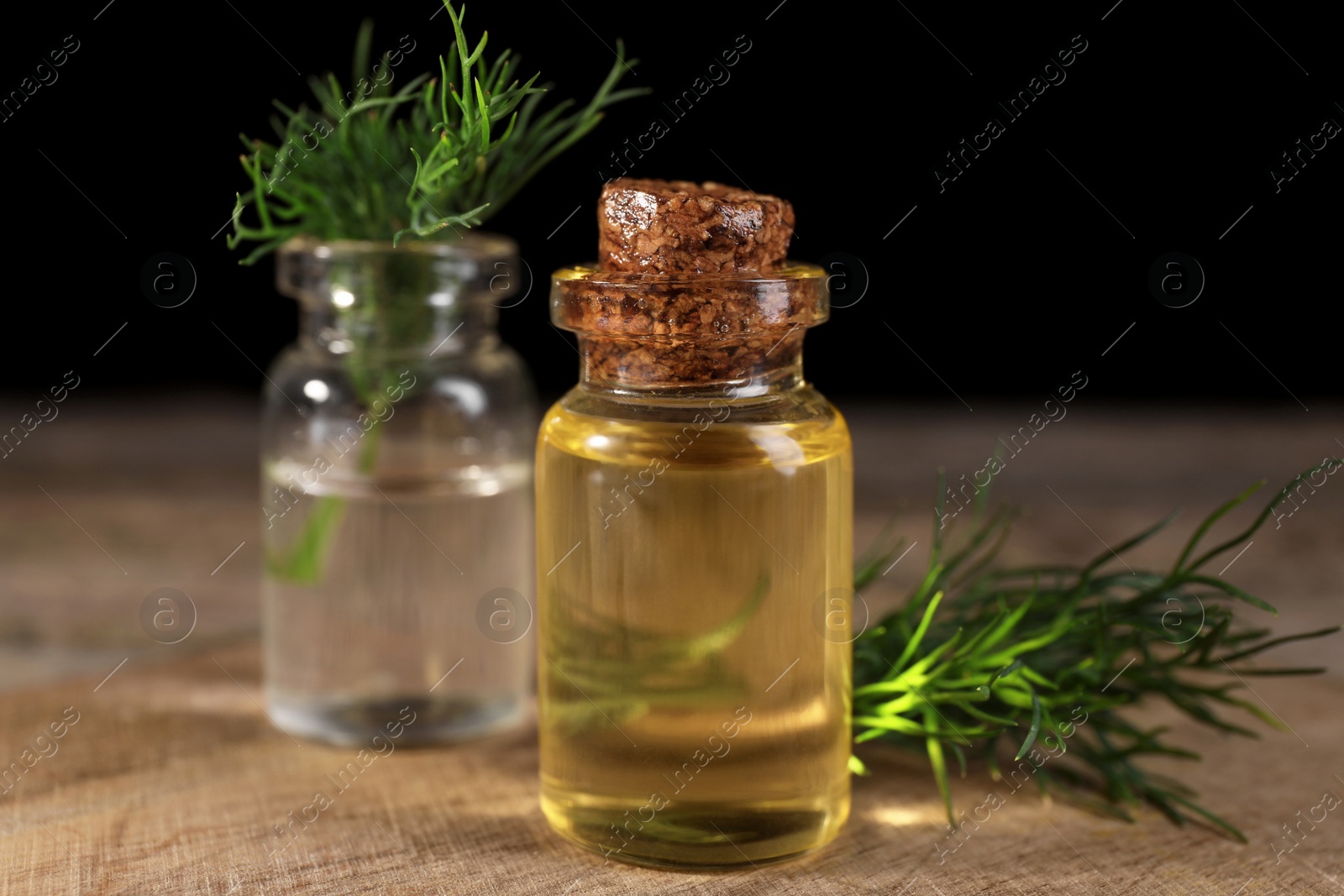 Photo of Bottles of essential oil and fresh dill on wooden table, closeup