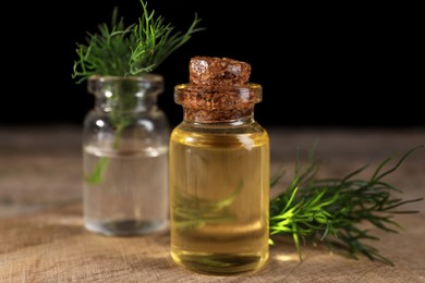 Photo of Bottles of essential oil and fresh dill on wooden table, closeup