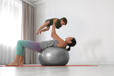 Young woman doing exercise with her son indoors. Home fitness