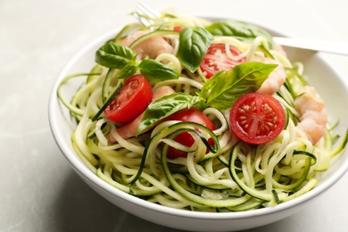 Delicious zucchini pasta with shrimps, cherry tomatoes  and basil in bowl on light grey table, closeup