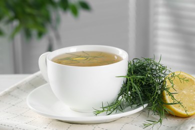 Aromatic herbal tea, fresh tarragon sprigs and lemon on table, closeup