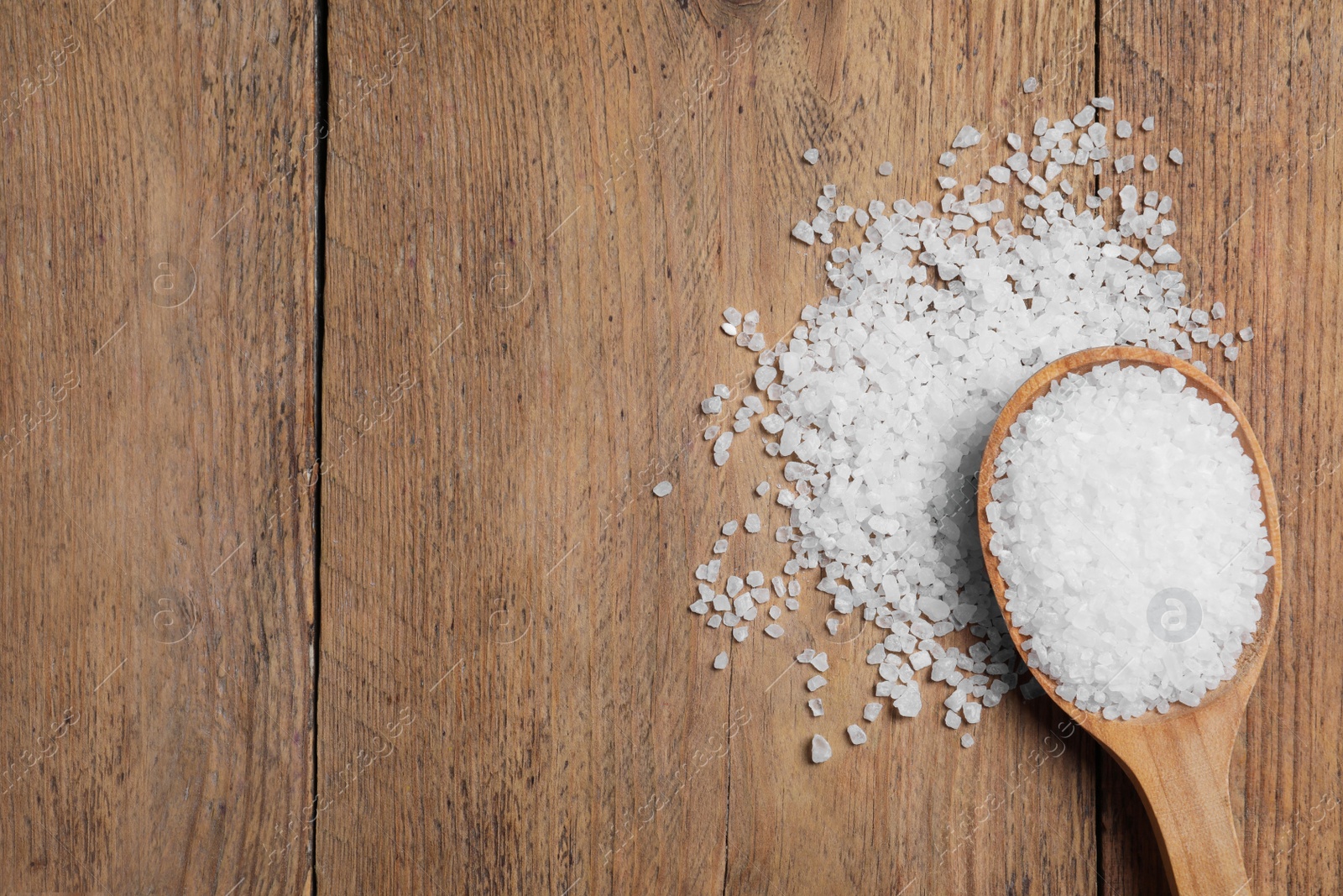 Photo of Spoon and heap of natural sea salt on wooden table, top view. Space for text