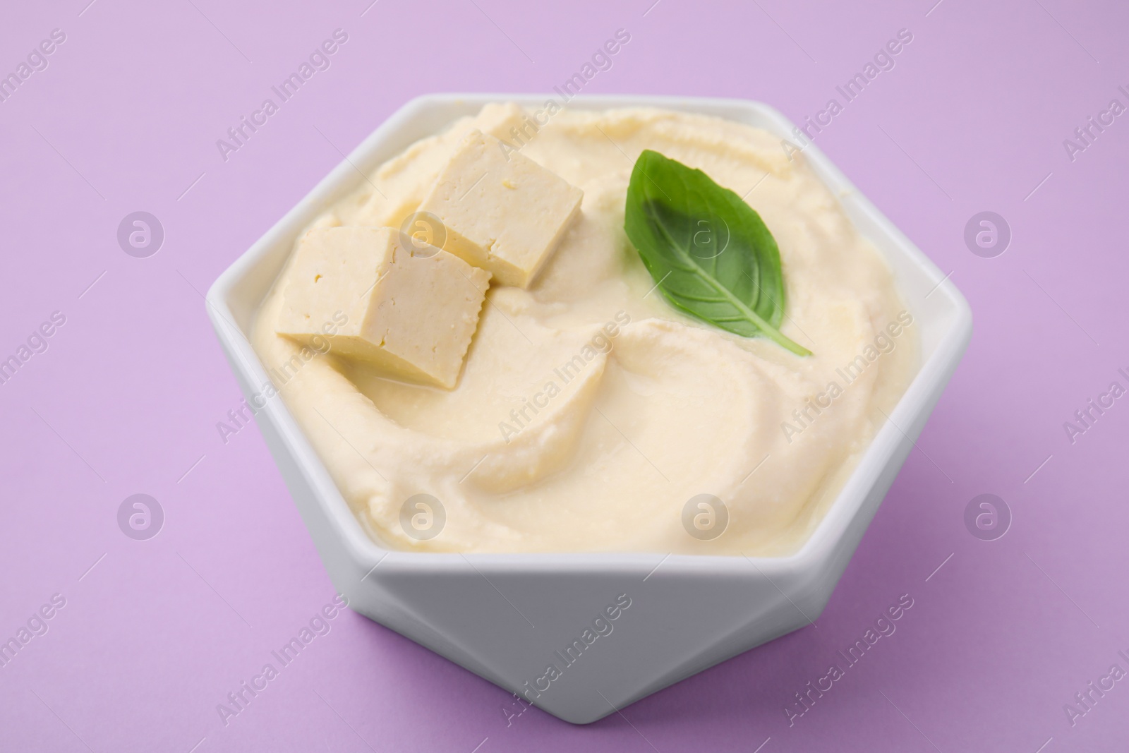 Photo of Delicious tofu sauce and basil leaf in bowl on violet background, closeup