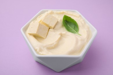 Photo of Delicious tofu sauce and basil leaf in bowl on violet background, closeup