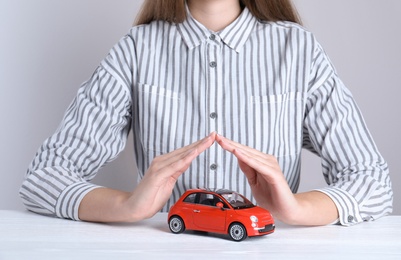 Photo of Insurance agent covering toy car on table, closeup