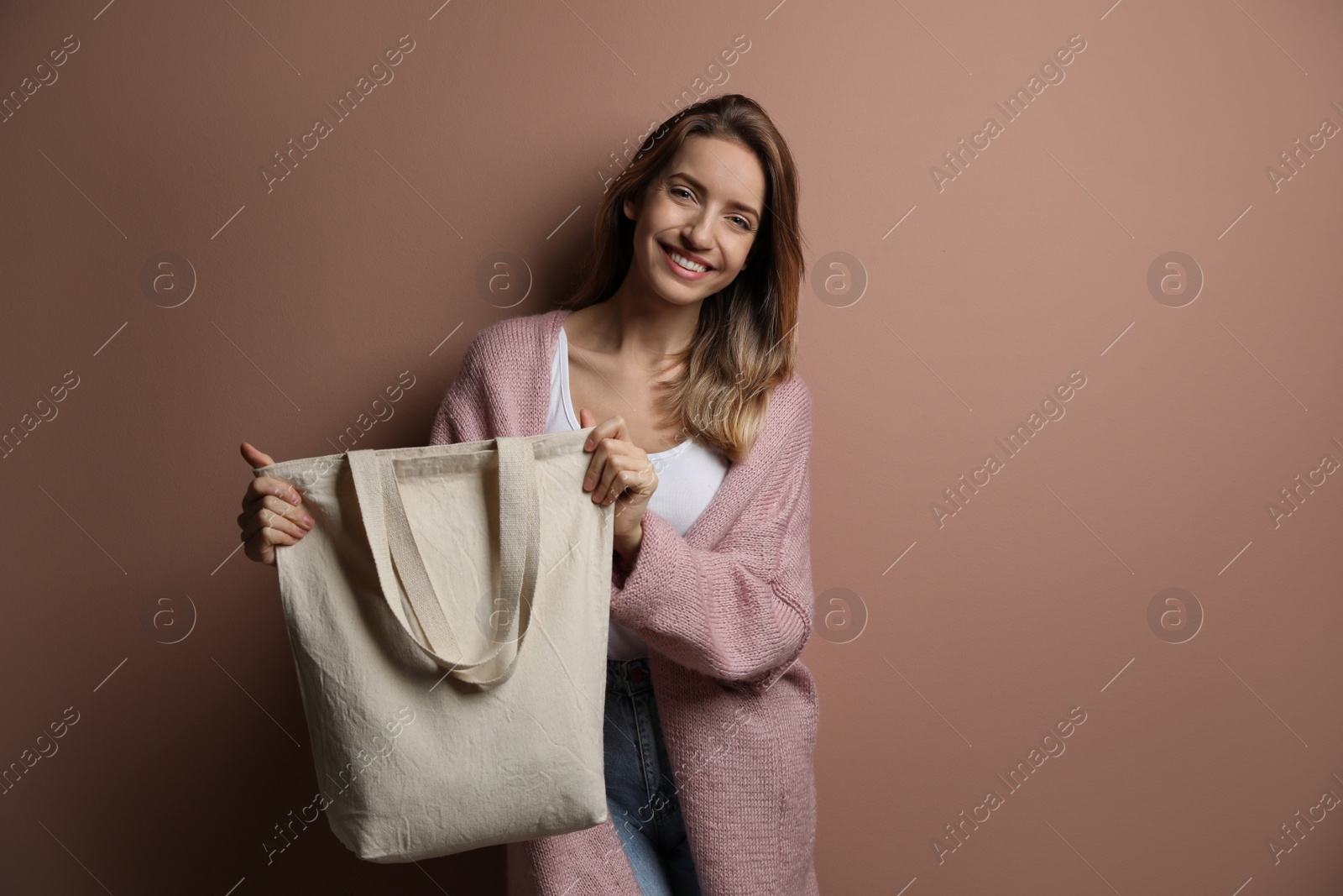 Photo of Happy young woman with blank eco friendly bag against light brown background