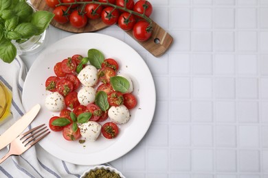 Photo of Tasty salad Caprese with tomatoes, mozzarella balls and basil served on white tiled table, flat lay. Space for text
