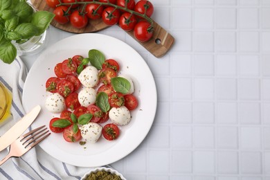 Tasty salad Caprese with tomatoes, mozzarella balls and basil served on white tiled table, flat lay. Space for text