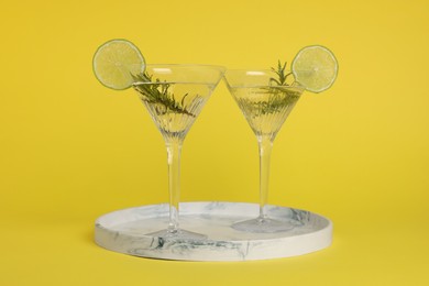 Photo of Martini glasses of refreshing cocktail with lemon slices and rosemary on yellow background