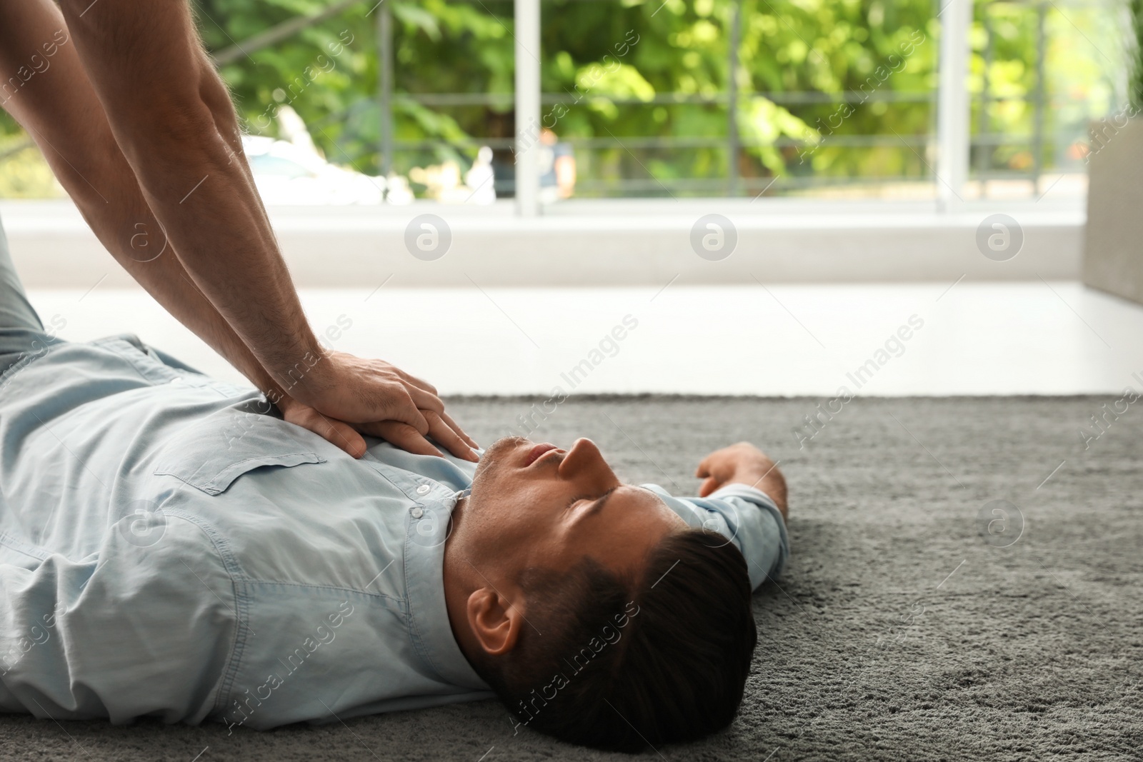 Photo of Passerby performing CPR on unconscious man indoors. First aid