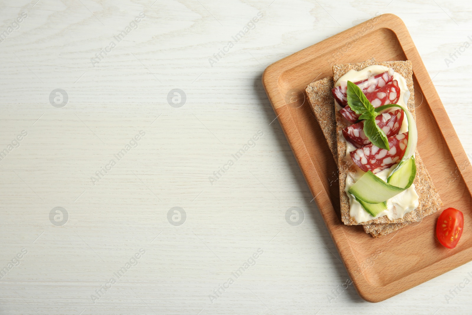 Photo of Fresh rye crispbreads with salami, cream cheese and cucumber on white wooden table, top view. Space for text