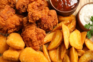 Photo of Tasty deep fried chicken pieces and nuggets with garnish as background, top view
