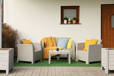 Beautiful rattan garden furniture, soft pillows, blanket and yellow chrysanthemum flowers outdoors