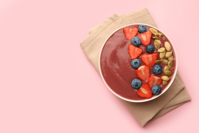 Photo of Bowl of delicious smoothie with fresh blueberries, strawberries and pumpkin seeds on pale pink background, top view. Space for text