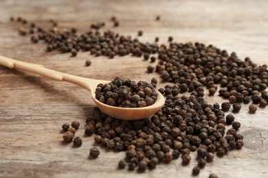Photo of Spoon and black peppercorns on wooden table