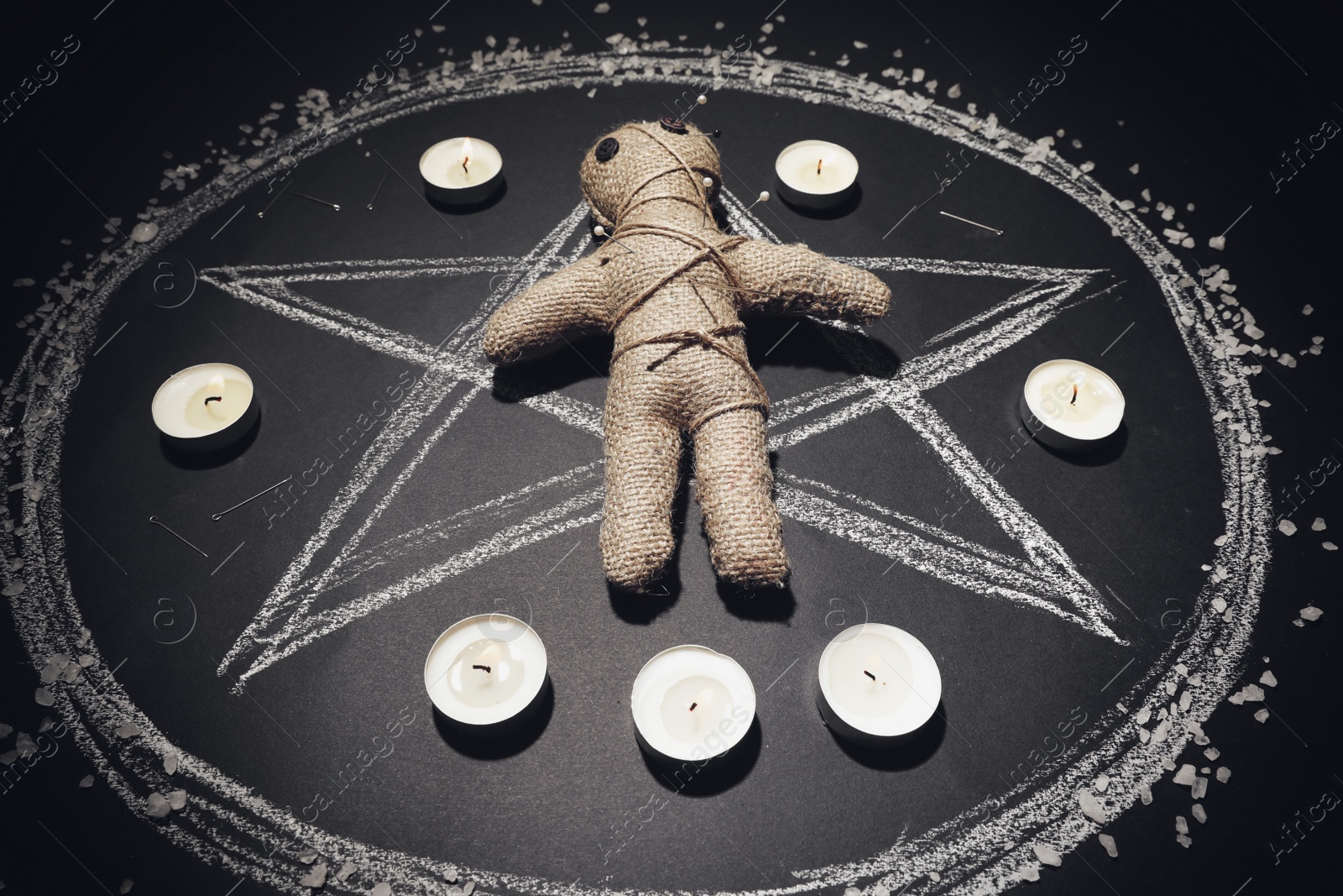 Photo of Voodoo doll pierced with pins and candles in pentagram on black table