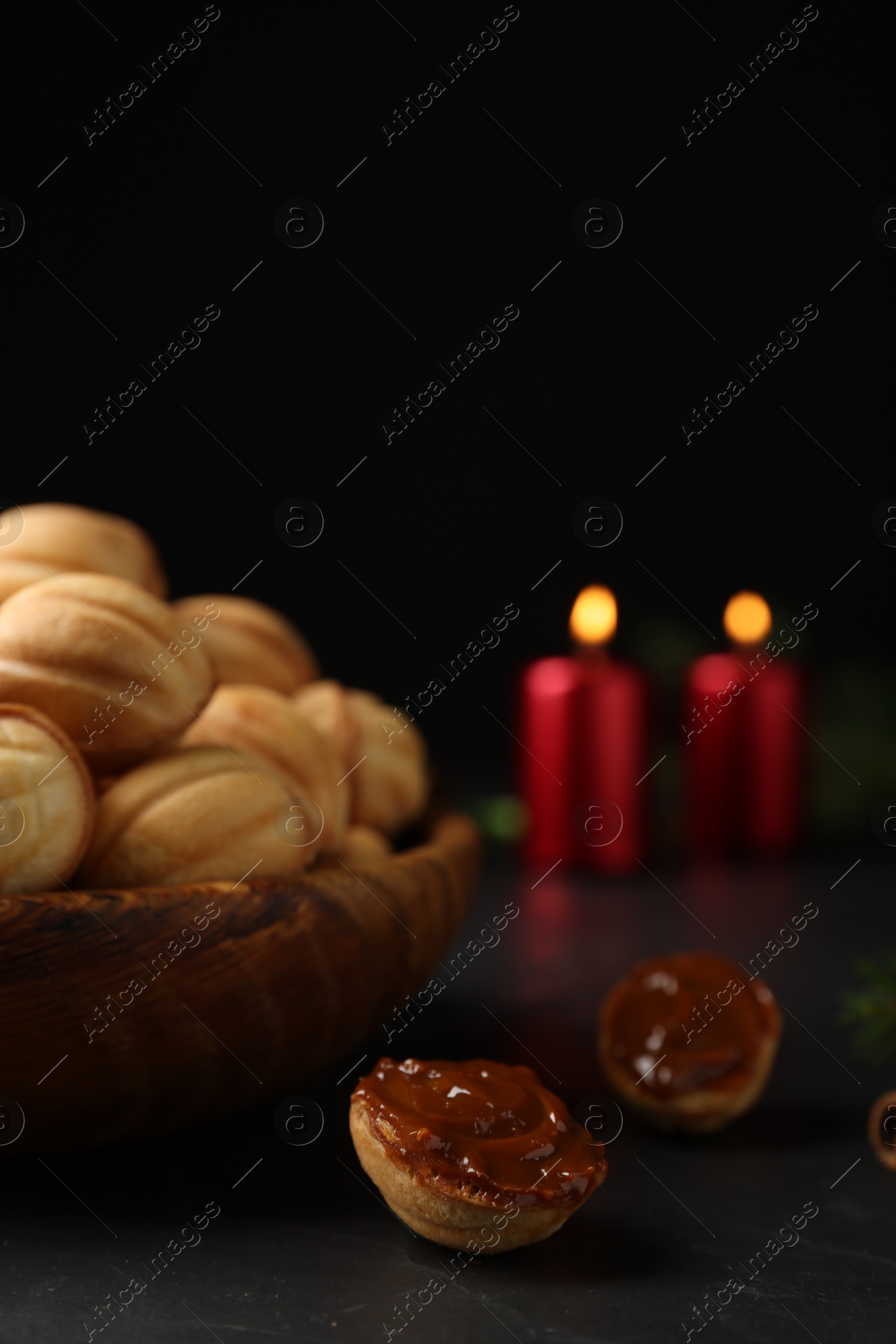 Photo of Homemade walnut shaped cookies with boiled condensed milk and candles on black table, space for text