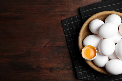 Photo of Many fresh raw chicken eggs in bowl on wooden table, flat lay. Space for text