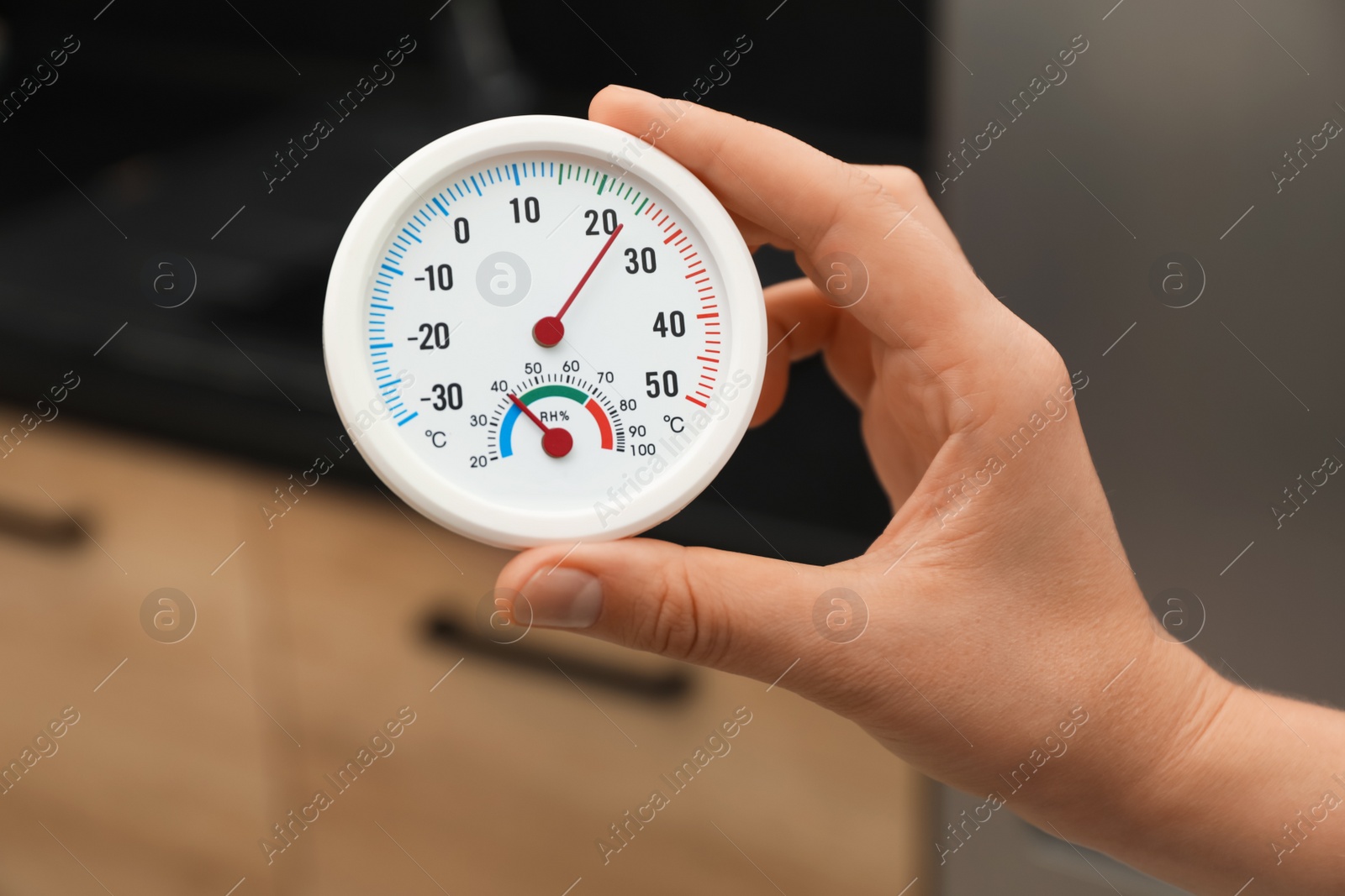 Photo of Woman holding round hygrometer with thermometer at home, closeup