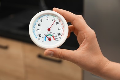 Photo of Woman holding round hygrometer with thermometer at home, closeup