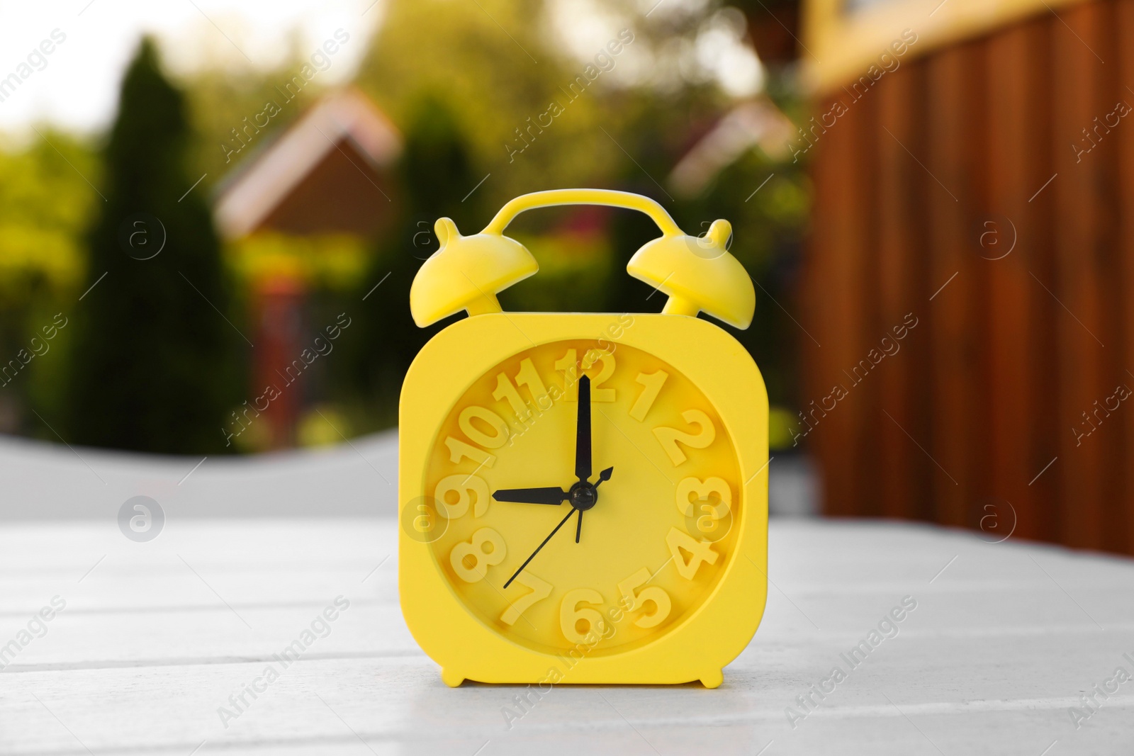 Photo of Yellow alarm clock on white wooden table outdoors at sunny morning