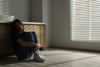 Photo of Sad young woman sitting on floor in bathroom, space for text