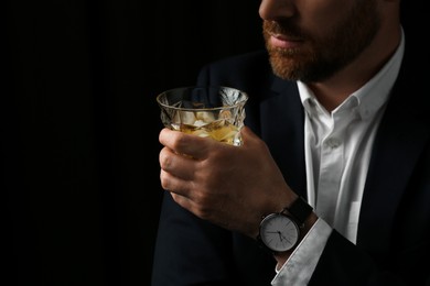 Man holding glass of whiskey with ice cubes on black background, closeup. Space for text