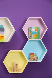 Photo of Hexagon shaped shelves with toys on purple wall. Interior design