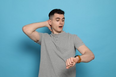 Photo of Emotional young man checking time on light blue background. Being late concept