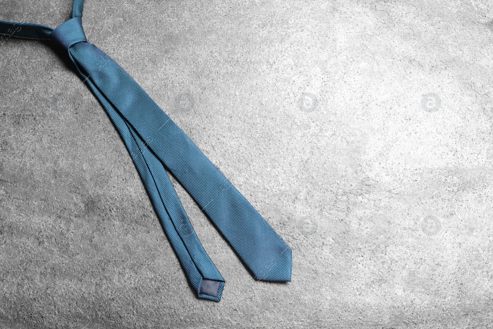 Photo of One blue necktie on grey textured background, top view. Space for text
