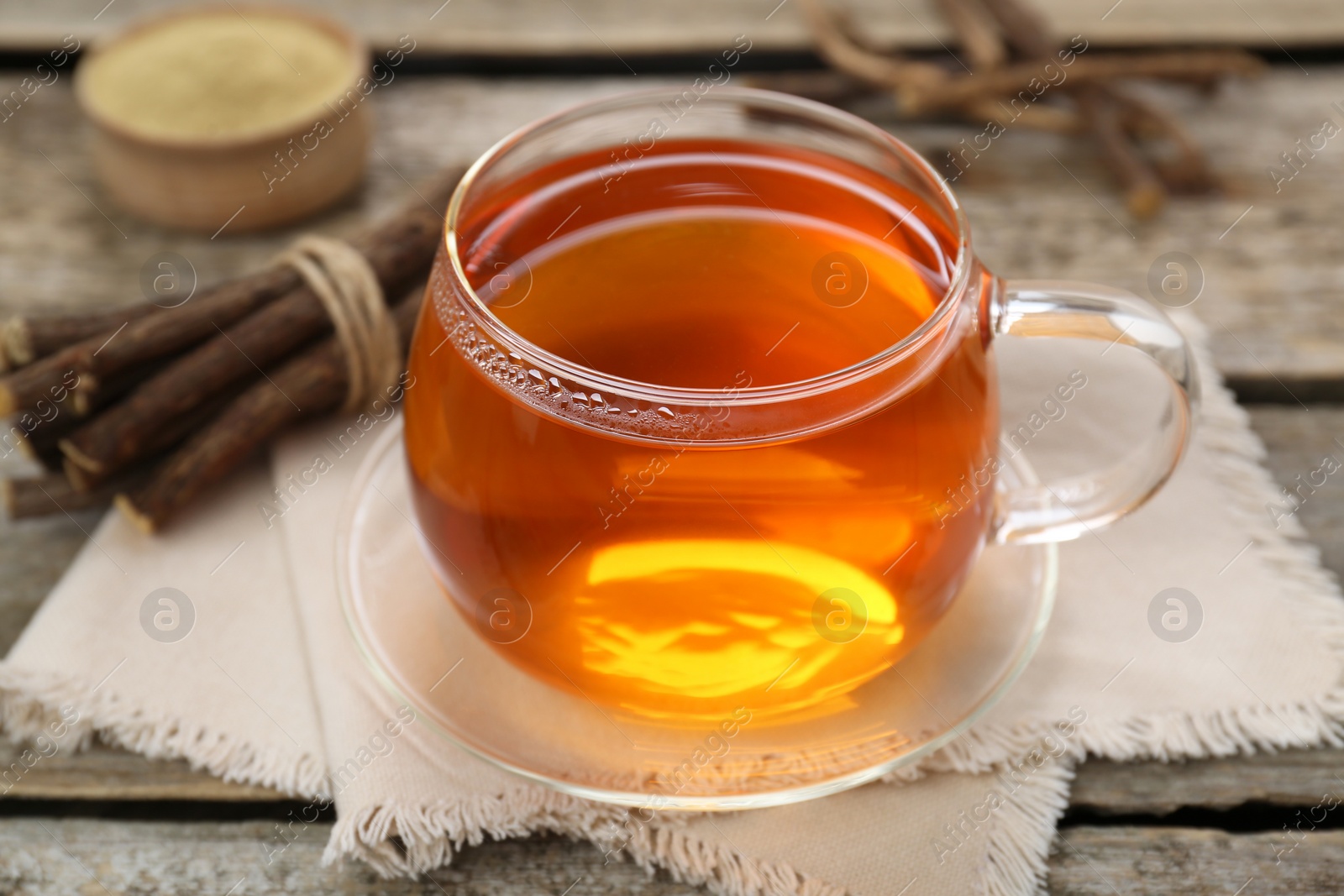 Photo of Aromatic licorice tea in cup and dried sticks of licorice root on wooden table, closeup