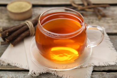 Photo of Aromatic licorice tea in cup and dried sticks of licorice root on wooden table, closeup