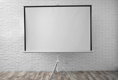 Photo of Projection screen near white brick wall indoors. Space for design