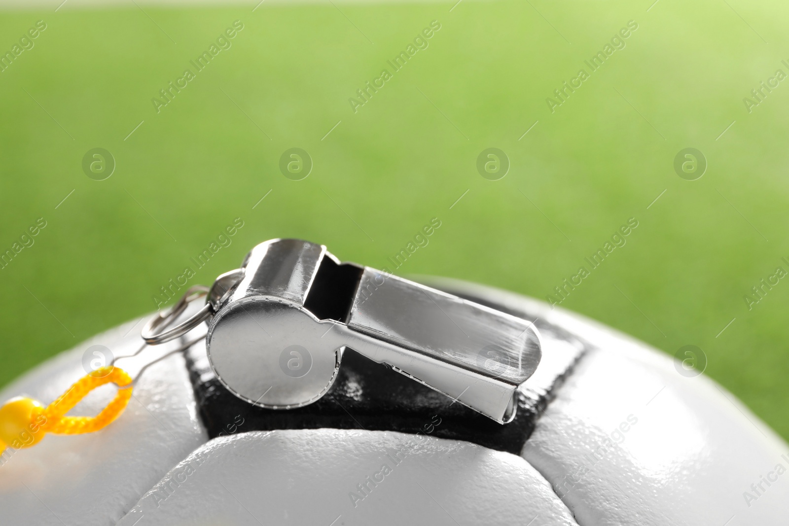 Photo of Football referee equipment. Soccer ball and metal whistle on green background, closeup with space for text