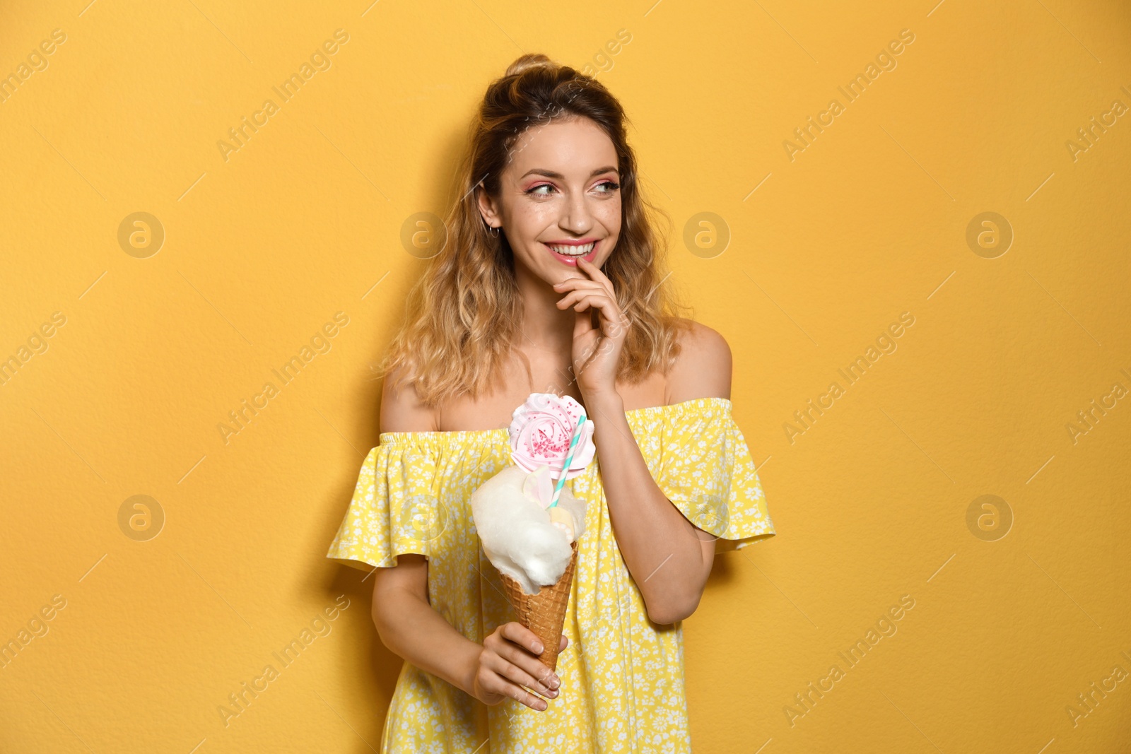 Photo of Portrait of young woman holding cotton candy dessert on yellow background