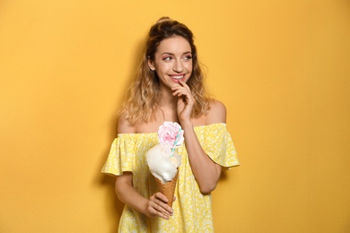 Portrait of young woman holding cotton candy dessert on yellow background