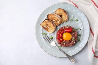 Tasty beef steak tartare served with yolk, toasted bread and other accompaniments on white table, top view. Space for text