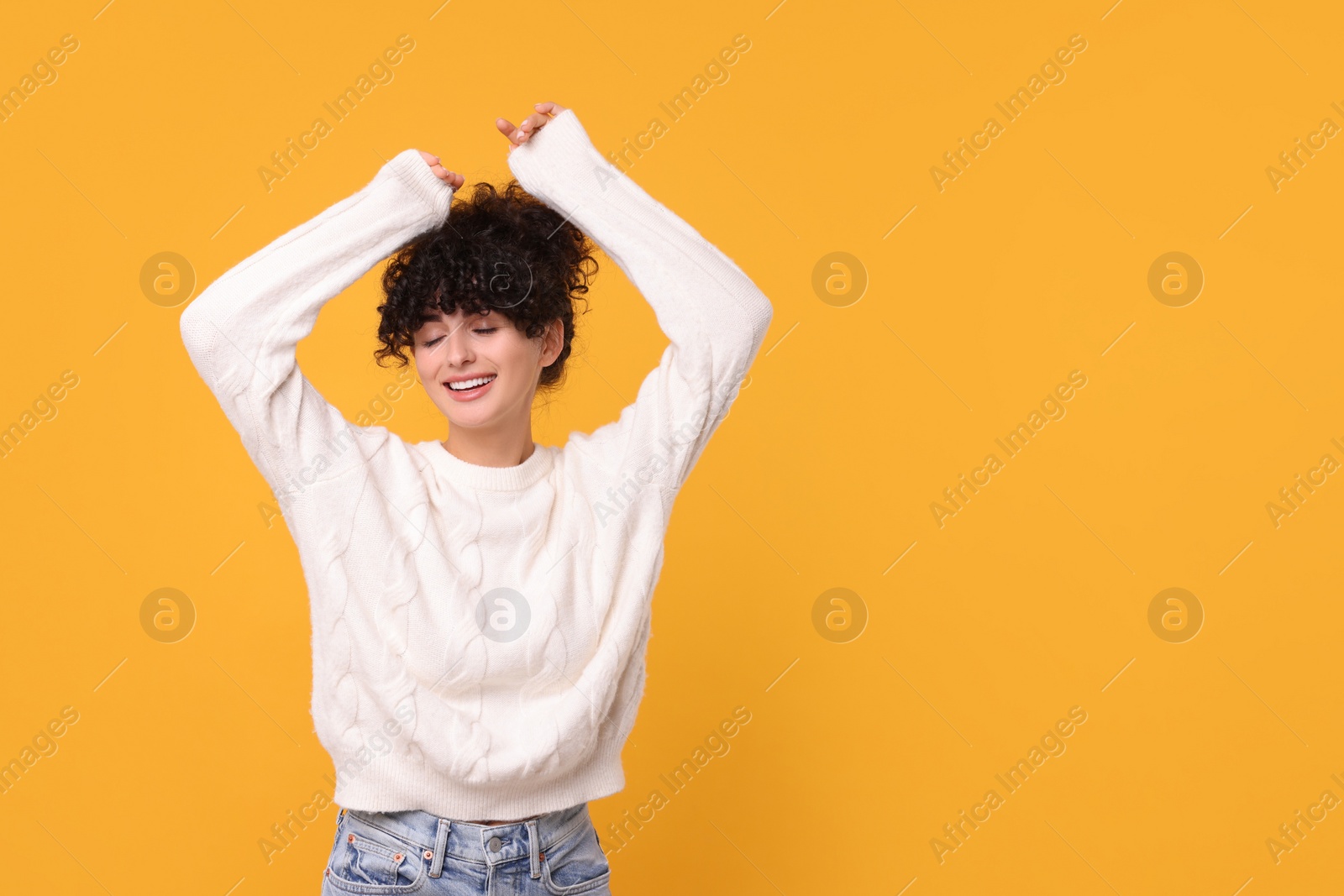 Photo of Happy young woman in stylish white sweater on yellow background, space for text