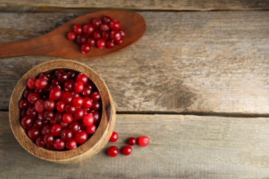 Cranberries in bowl and spoon on wooden table, top view. Space for text