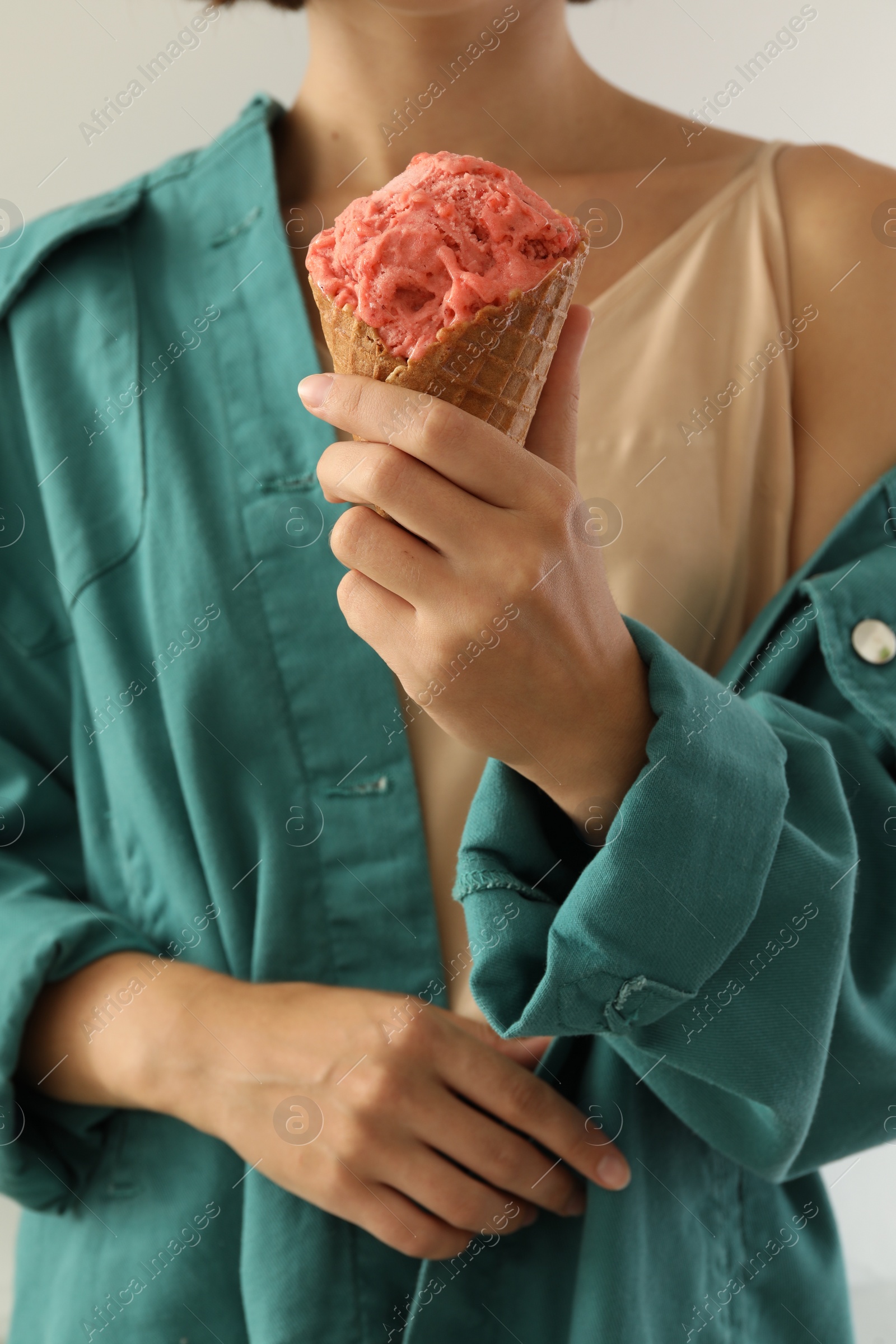 Photo of Woman holding pink ice cream in wafer cone on light grey background, closeup