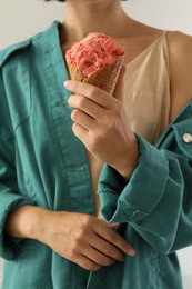 Woman holding pink ice cream in wafer cone on light grey background, closeup