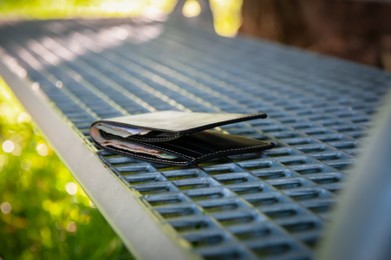 Photo of Black wallet on metal bench outdoors. Lost and found