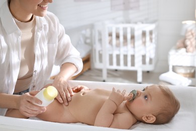 Mother with bottle of dusting powder near her cute baby at home, closeup