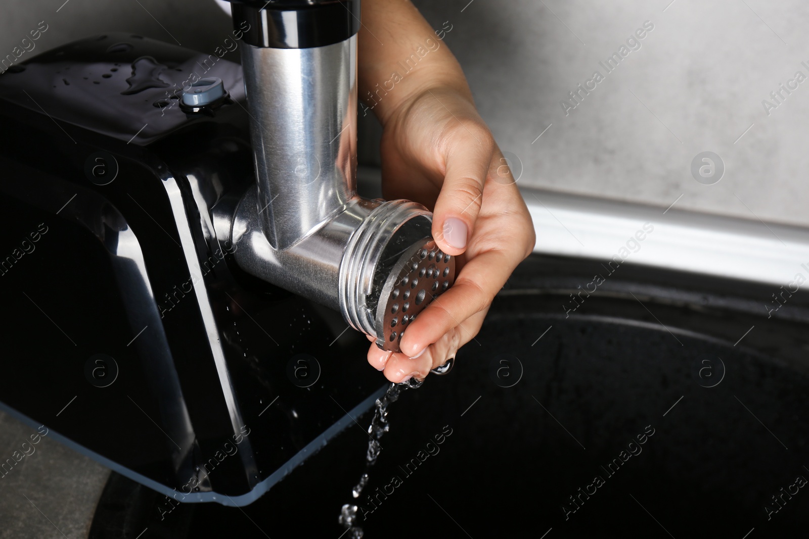 Photo of Woman washing electric meat grinder in kitchen sink indoors, closeup