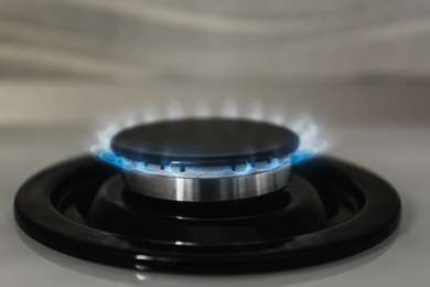 Photo of Gas burner with blue flame on modern stove, closeup